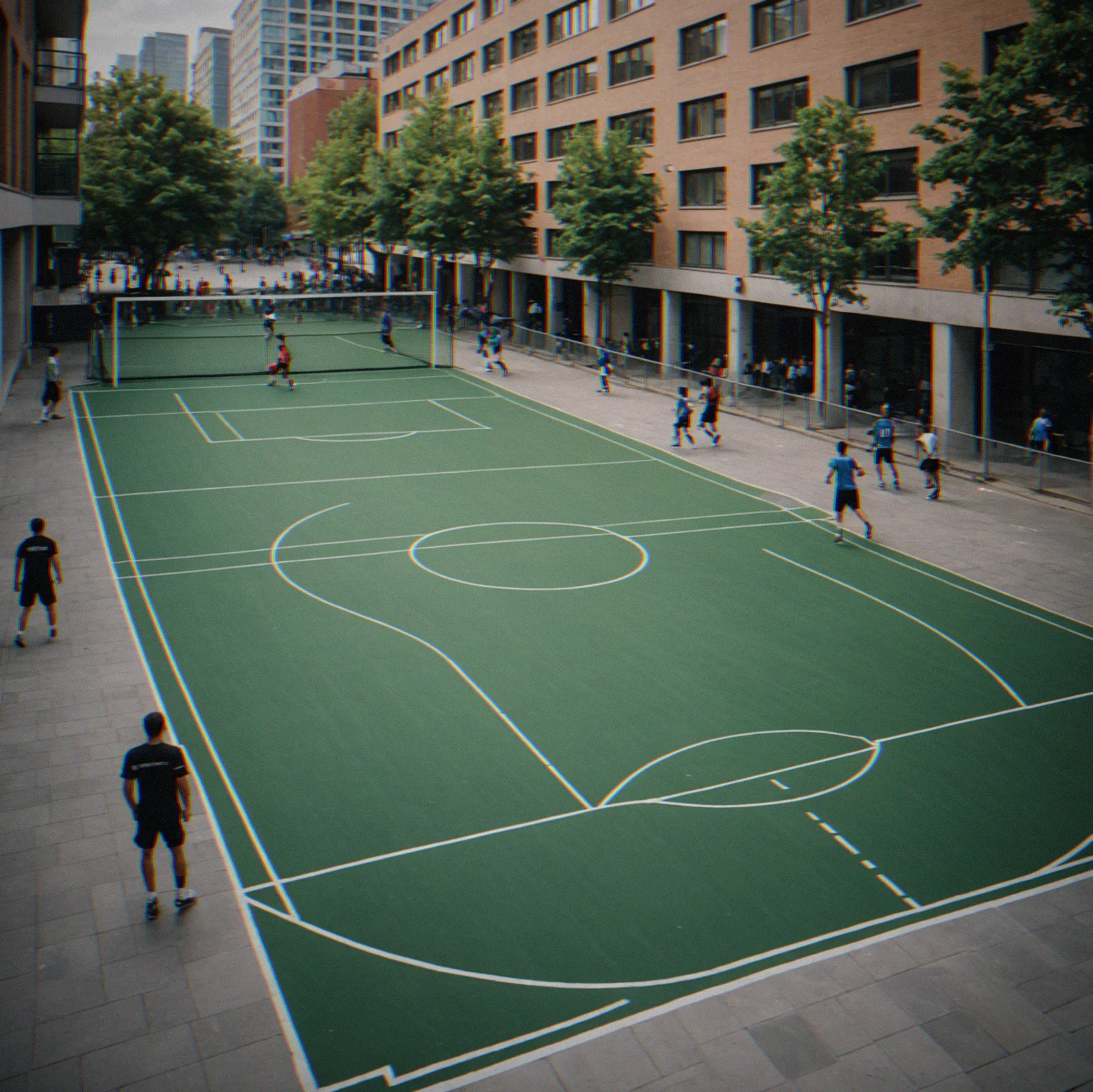 Street-level view of a futsal court situated between city buildings with transit nearby